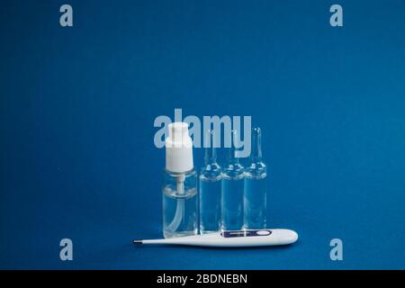 Thermometer and transparent ampoules with medicine, antibacterial hand gel on a blue background. Health conservation concept. Stock Photo