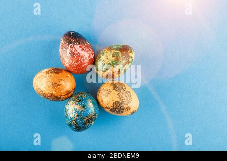 Five easter eggs painted in blue, green, red and yellow lie in a circle. Painted easter eggs on a blue background with light. Flat lay. Copy space. Stock Photo