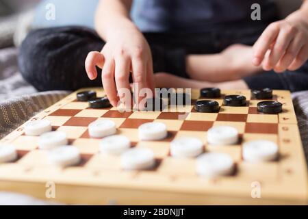 Stay at home Quarantine concept. Young kid hands playing checkers table game on bed. Board game and kids leisure concept. Family time.  Stock Photo
