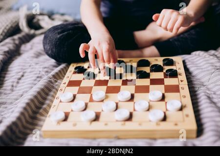 Young kid hands playing checkers table game on bed. Stay at home Quarantine concept. Board game and kids leisure concept. Family time.  Stock Photo