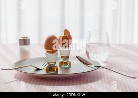 view of two boiled eggs on ceramic dark plate over a checkered tablecloth background for breakfast, diet food concept Stock Photo