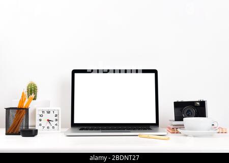 Workplace with laptop computer white blank screen on work table front view, modern gadgets. Laptop on a table over white wall. Stock Photo