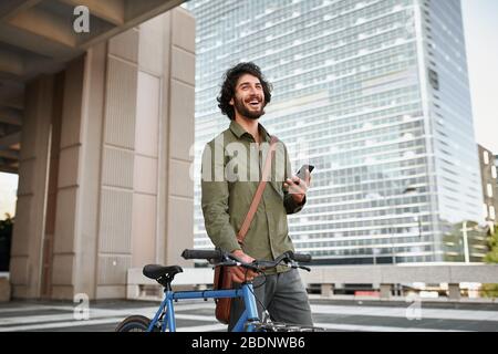 Low angle view of young man with cycle using smartphone while standing Stock Photo