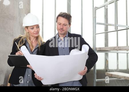 man and woman architects or engineers work together discussing with blueprint in the inside the construction building site Stock Photo