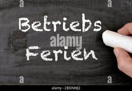 a person writing the german words Betriebsferien on a chalkboard, translate company holidays Stock Photo