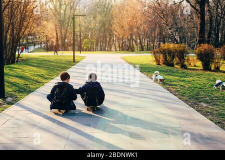 Two little boys sitting on their skateboards in the park Stock Photo