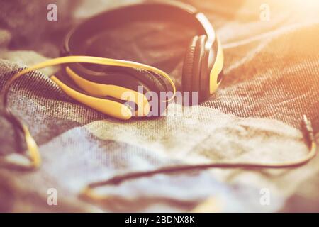 On a soft wool plaid blanket, yellow headphones with a microphone lie in the sunlight of a bright day. Time for inspiration. Stock Photo
