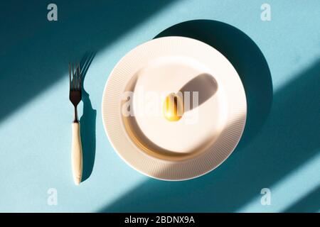 Golden easter egg lies on white plate on blue background close to fork. Easter concept. Flatlay. Stock Photo