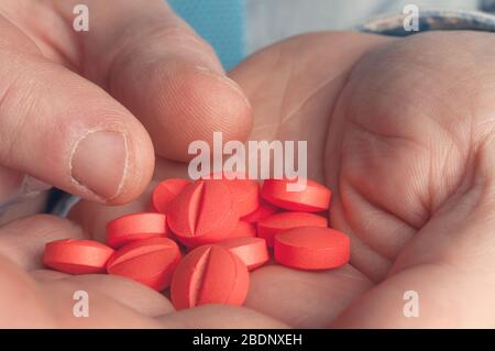 A doctor's hand takes a pill to be administered to the patient by a hand full of red pills Stock Photo