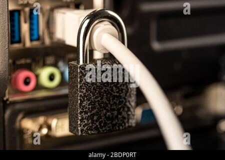 Closed lock hanging on a network cable plugged into a computer. The concept of security or blocking the Internet or the safety of personal data. Antiv Stock Photo