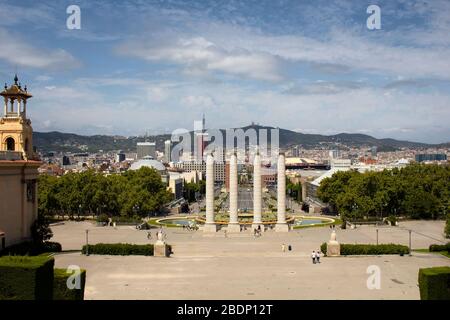 View of people walking at a square called 'Placa de les Cascades'. 'Font Magica de Montjuic' and Barcelona city are in the view. It is a sunny summer Stock Photo