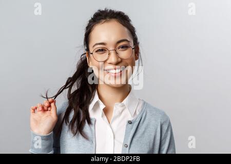 Close-up portrait of flirty, enthusiastic brunette asian female in glasses, beaming smile, roll strand of hair between fingers as coquettish talking Stock Photo