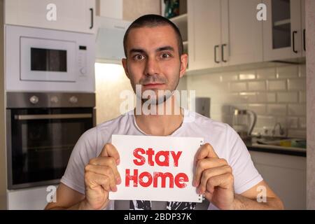 Young man with no mask is staying at home during the COVID-19 lockdown. Holding paper stay home text. Social media campaign concept for coronavirus pr Stock Photo
