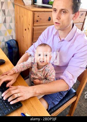 A higher education employee working from home WFH during the Covid 19 pandemic assisted by his seven month old daughter. England UK Stock Photo