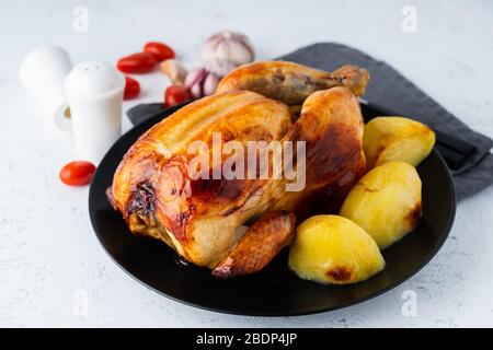 Grilled whole chicken in black plate on white table, baked meat with potatoes. Side view Stock Photo