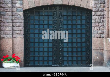 Closed forged gate at christian catholic church and red flowers in flowerbed Stock Photo