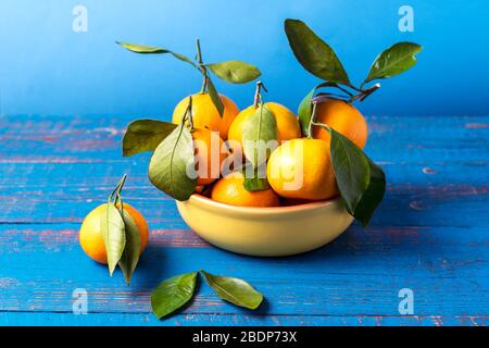 Flat lay view of Orange ripe mandarins or tangerines fruit with green leaves, on blue and white napkin, over rustic blue background. Stock Photo