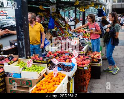 Locals stop to pick up fruits and vegetables from a street vendor at his produce stand in the City of Westminster, Greater London. Stock Photo