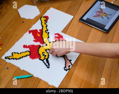 Hand of young boy placing Hama beads to finish a design of a Moltres Pokemon during Lockdown Stock Photo