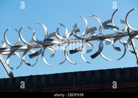Tall and high brick wall with barbed / razor wire on the top of it, for ...