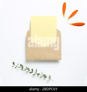 Kraft envelope and empty card with flower leaves, eucalyptus leaves on white background. Floral composition, flat lay, top view, copy space Stock Photo