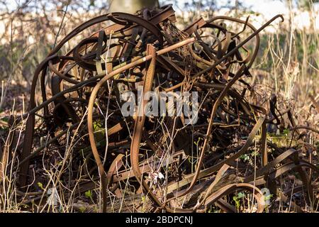 Scrap metal pile of twisted rusty old farm metalwork fencing and hay bale cage all rolled up into a pile in semi woodland farmland Stock Photo