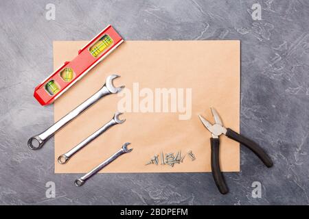 Different hand tools for construction, repair- pliers, level tool, screw, spanner on craft envelope with free space on grey background. Top view, flay Stock Photo