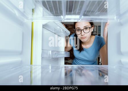 Sad woman looking into her empty fridge with no groceries Stock Photo