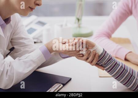 Young girl with fractured wrist in the doctor's office, the pediatrist is checking her bandage and visiting her, kids and healthcare concept Stock Photo