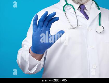 doctor’s hand is wearing a blue sterile rubber glove holding an object, blue background, close up Stock Photo