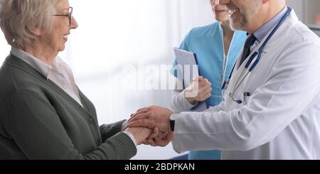 Friendly professional doctor holding a senior patient's hands and supporting her: care, assistance and medicine concept Stock Photo