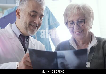 Professional radiologist examining an x-ray image with a senior patient during a visit at the clinic, the doctor is pointing and giving advices Stock Photo