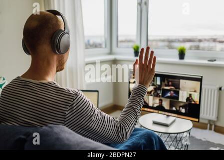 Man in headphones working from home. Having a video call meeting with his team on big monitor Stock Photo