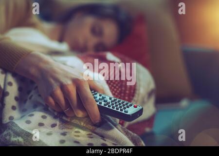 Woman falling asleep on the sofa at home while watching TV, she is holding the remote control Stock Photo