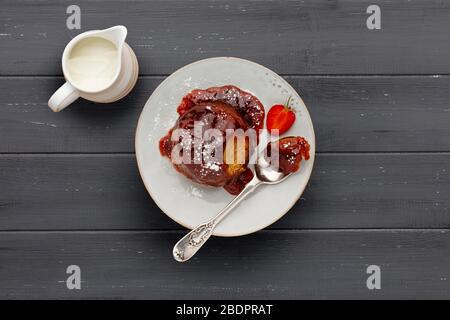 Strawberry sponge cake, with a sticky strawberry sauce, on a white plate with a spoon and a jug of cream, on a dark grey wooden surface with space for Stock Photo