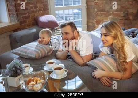 Tea time. Mother, father and son at home having fun, comfort and cozy, love concept. Looks happy, cheerful and joyful. Beautiful caucasian family. Spending time together, playing, watching cinema. Stock Photo