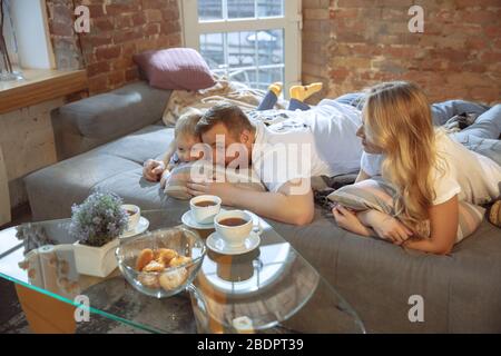 Tea time. Mother, father and son at home having fun, comfort and cozy, love concept. Looks happy, cheerful and joyful. Beautiful caucasian family. Spending time together, playing, watching cinema. Stock Photo