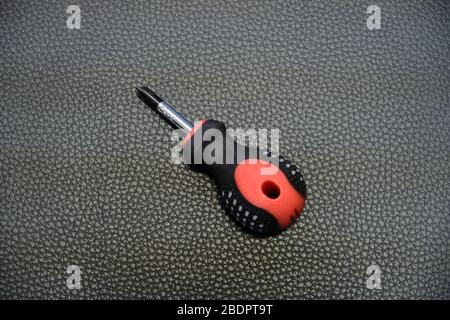 Black and red short crosshead screwdriver on black leather background Stock Photo