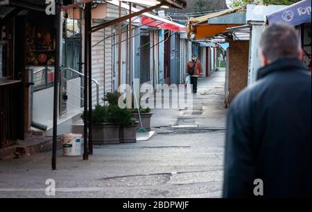 Woman wearing protective face mask is walking in empty market lane with abandoned and deserted shops and small businesses closed down due to economic and industrial decline in the area during the Coronavirus Pandemic of Covid-19 in Sofia Bulgaria Eastern Europe as of 2020 Stock Photo