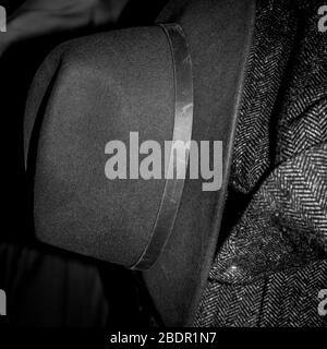 Retro felted hat and woolen overcoat of fishbone fabric hanging on a coat rack. Stock Photo