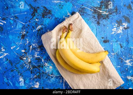 Banana fruits with tablecloth on blue textured background, top view copy space Stock Photo