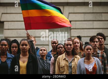 People participate in the pride parade. Multi-ethnic people in the city street with a woman waving gay rainbow flag. Stock Photo