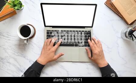 Top view image of businessman's hands typing on computer laptop keyboard with white blank screen that putting on marble texture table surrounded with Stock Photo