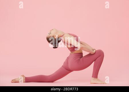 Young flexible woman doing stretching exercise over pink background Stock Photo