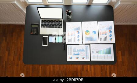 Top view image of Data analyst workplace. Computer laptop with white blank screen, Pencil holder, Calculator, Smartphone, Post it, Data sheets and Pen Stock Photo