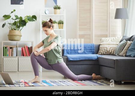 Young healthy woman watching sports training online and doing exercises in the living room at home Stock Photo