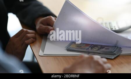 Cropped image of Businessman receiving money under the document paper after finished meeting or negotiation at table with the wooden table as backgrou Stock Photo