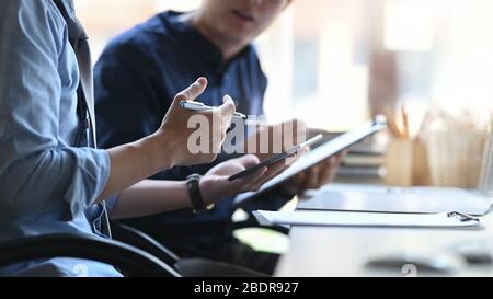 Cropped image of business developer team discussing/talking/meeting while sitting at the modern meeting table with orderly office as background. Stock Photo