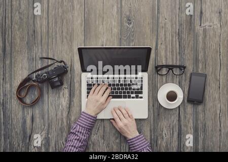 Hipster freelance working at office desk, he is networking and typing on a laptop, top view Stock Photo