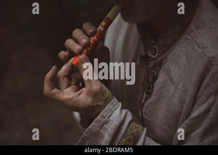 A man in a Russian national costume blows a handmade whistle. Stock Photo